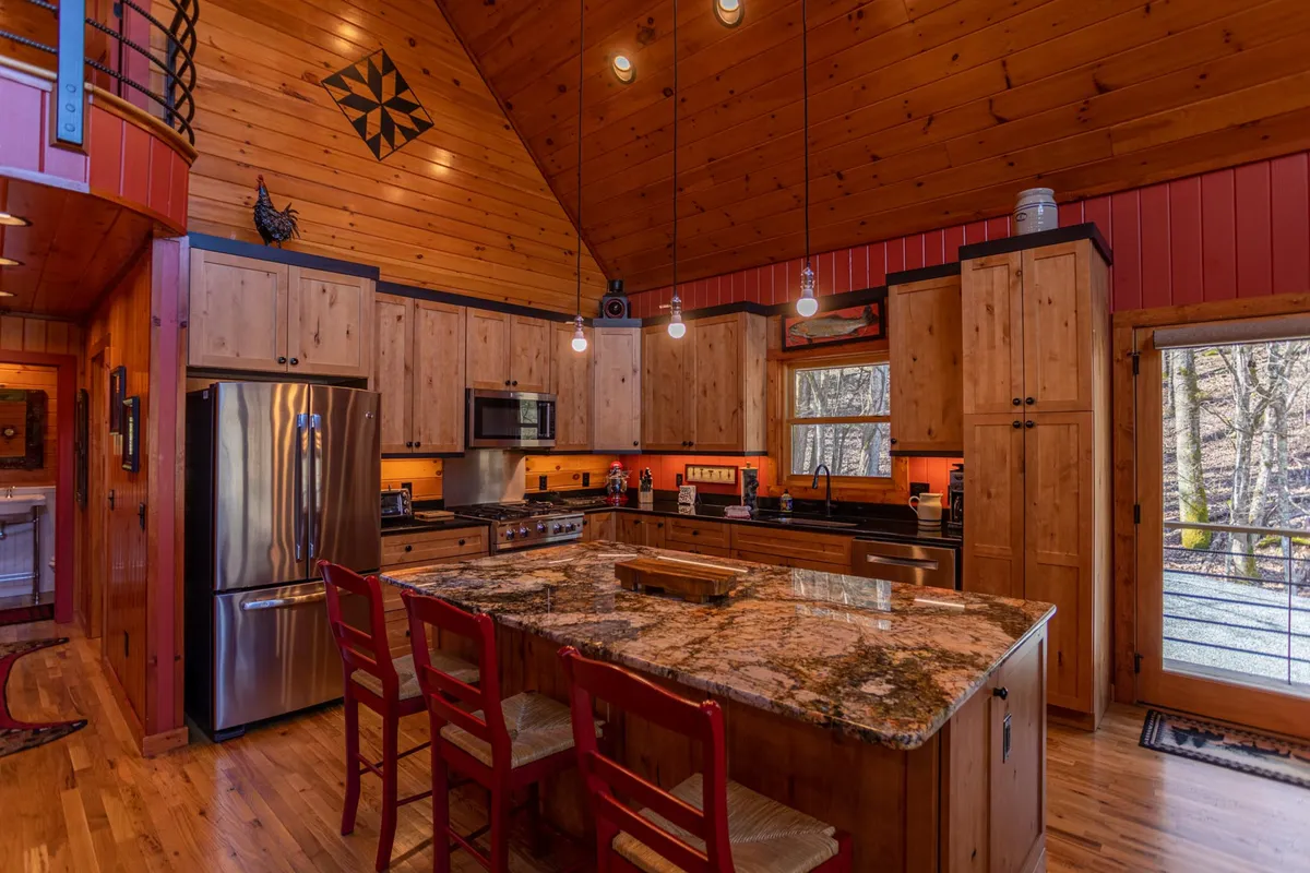 A spacious, light-filled kitchen anchored by a large granite island, with wooden cabinets and sizable windows. The open design connects visually to adjacent spaces, illustrating a practical and social culinary environment.