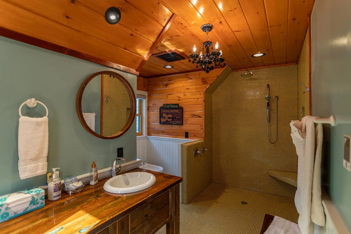 A tranquil, elegantly designed bathroom featuring a wooden ceiling, chandelier, mirror, and sink, evoking a spa-like atmosphere.