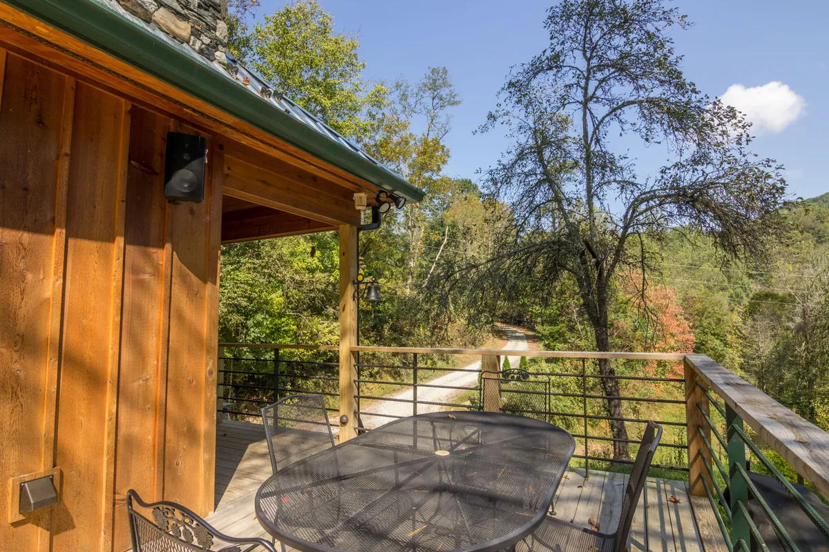 A large wooden deck with an outdoor dining table and chairs, surrounded by leafy trees. A pathway leads away from the deck, suggesting a direct link to private trails and further outdoor discovery.