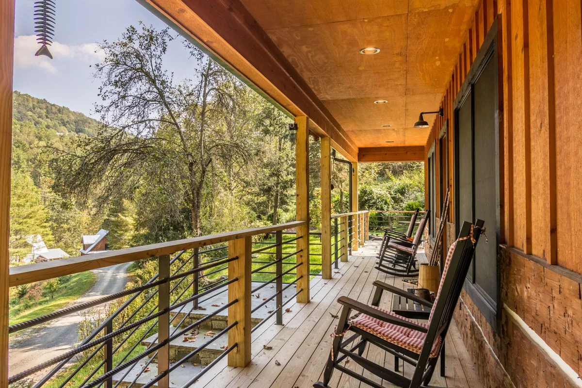 A tranquil exterior view featuring wooden rocking chairs lined up along a deck railing, overlooking a lush natural landscape. The scene suggests relaxation with the possibility of wildlife sightings and a sunset backdrop.