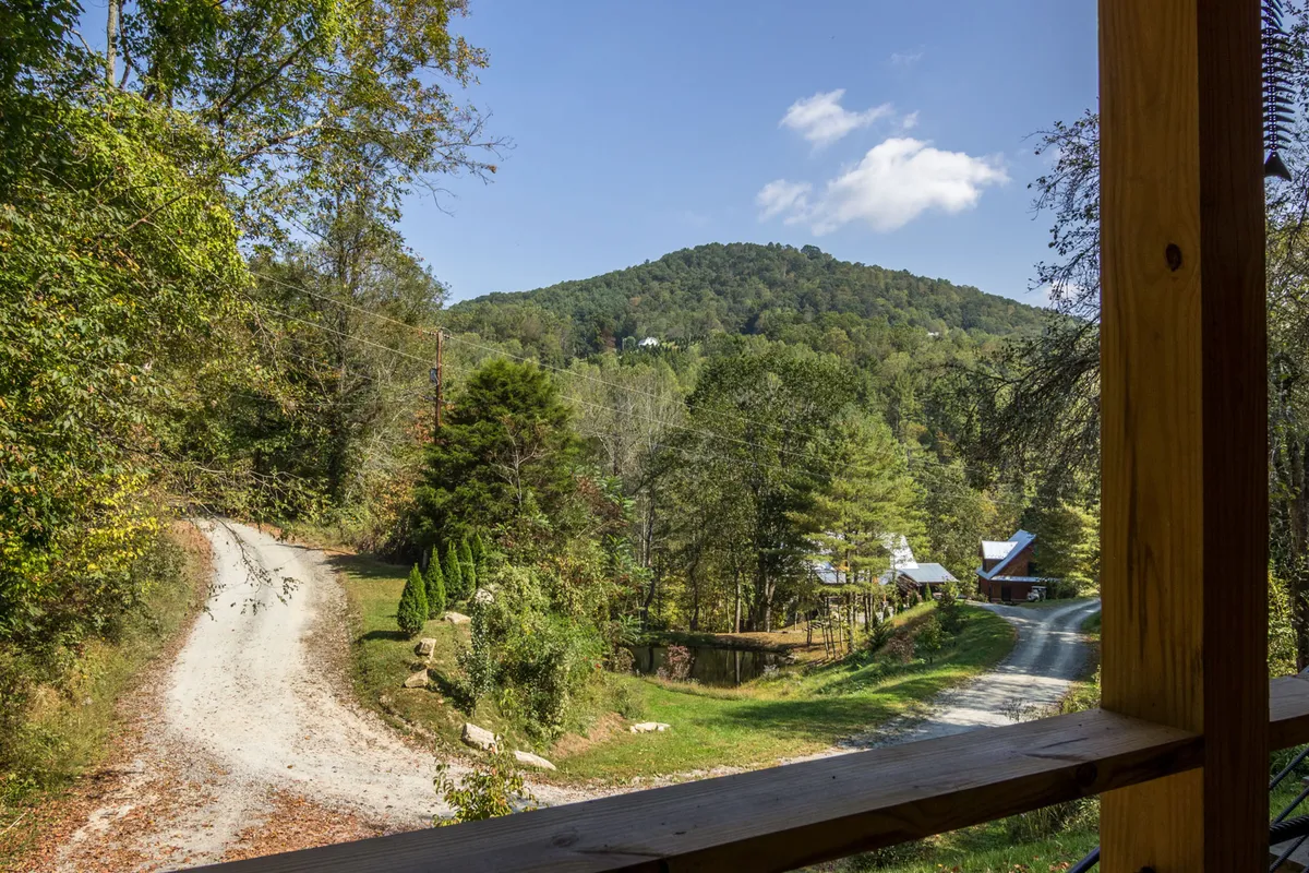 A sweeping view of mountain vistas, a dirt road, dense tree lines, and a distant farmhouse. The image captures the broader scenic context and sense of seclusion, perfect for exploration and quiet escapes.
