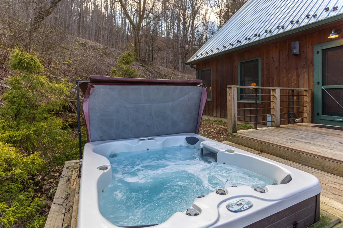 A sunken hot tub nestled on a wooden deck, surrounded by trees and the cabin’s rustic exterior. The scene exudes relaxation, inviting guests to soak while enjoying views of the natural surroundings.