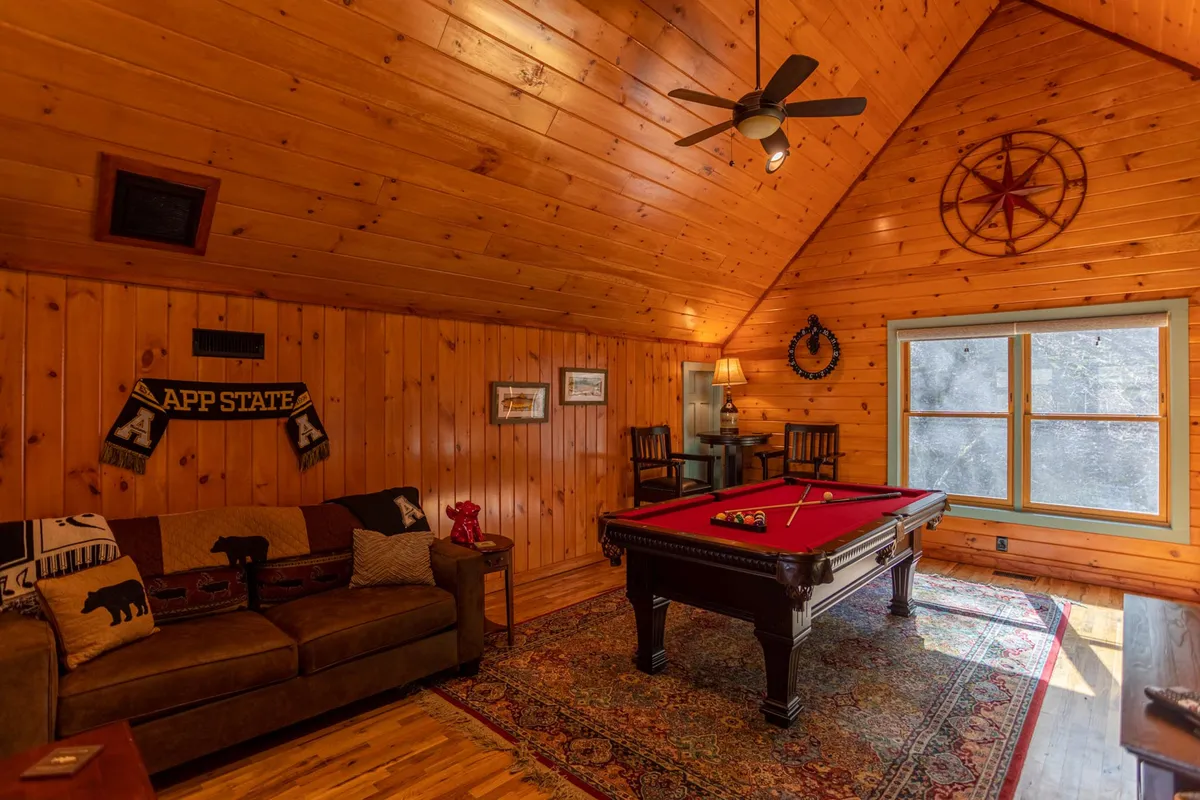 A bright and friendly space with a pool table, plush sofa, wall decorations, and a large window offering natural light. The layout feels open and inviting, ideal for both socializing and relaxing.